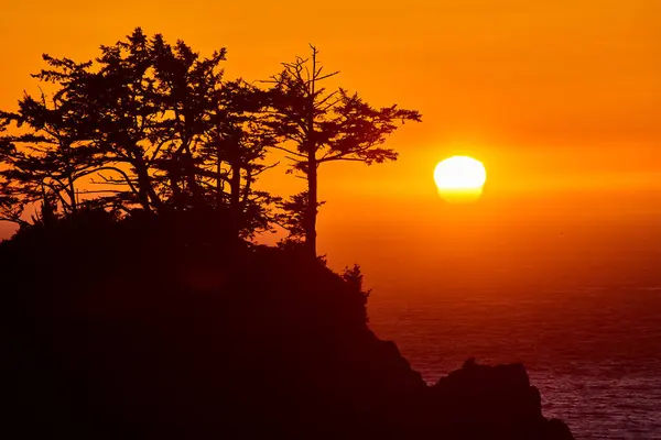 stock image Sunset over Arch Rock in Samuel H. Boardman State Scenic Corridor, Brookings, Oregon. Experience the breathtaking silhouette of rugged cliffs and dense trees against a vividly colored sky and serene