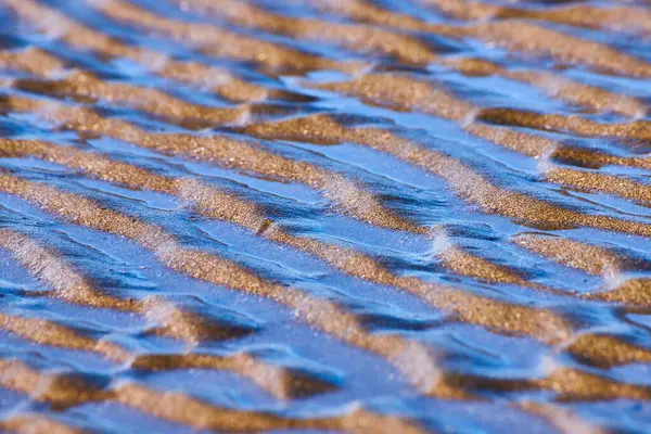 stock image Golden-brown wet sand patterns at Whaleshead Beach, Brookings, Oregon, reflect a soft blue hue during the blue hour. The wavy textures create a serene and tranquil coastal scene perfect for relaxation