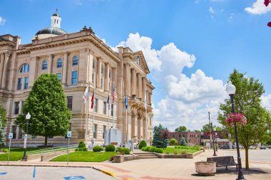 Huntington, Indiana 'daki görkemli neoklasik adliye binası. Parlak mavi gökyüzü ve gür yeşillik çerçevesi tarihi bina bayraklar, sokak lambaları ve bir savaş anıtı ile süslenmiştir.