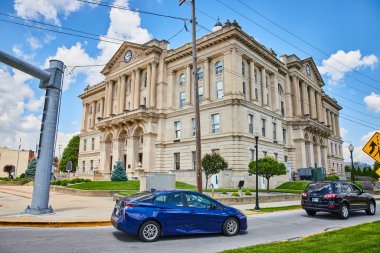 Stately courthouse with classical architecture in downtown Huntington, Indiana. A blend of historic elegance and urban life, featuring tall columns, a prominent clock, and city elements like cars and clipart