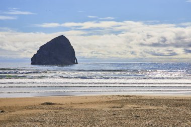 Pasifik City, Oregon 'daki Cape Kiwanda' nın dingin güzelliğini görün. Bu sakin kıyı sahnesi, okyanustan yükselen görkemli bir kaya oluşumunu, el değmemiş bir kumsal ve parıldayan bir kumsalı içerir.