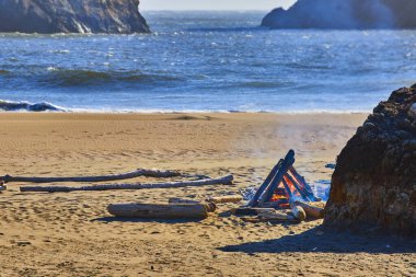 Serene evening at Harris Beach State Park, Oregon. A cozy campfire on sandy shores, framed by rugged rocks and a panoramic ocean view. Perfect for showcasing outdoor adventure and tranquility on the clipart