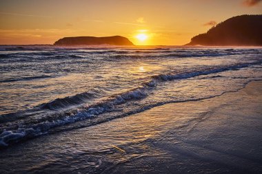 Golden sunset over Meyers Creek Beach in Oregon captures the serene beauty of the West Coast. Waves gently kiss the shore as the suns warm hues reflect off the water, creating a tranquil and clipart