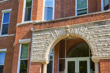 Charming brick and stone building with prominent archway at Huntington University, Indiana. Sunlit facade and lush greenery create a warm, inviting atmosphere suitable for themes of education clipart