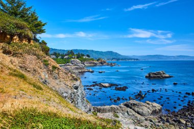 Brookings, Oregon 'daki Chetco Point Parkı' nda sakin bir sahil manzarası. Engebeli uçurumlar, sakin mavi sular ve yemyeşil bir körfez uzak kasaba manzaralı sakin bir körfez, dokunulmamış güzellikleri gözler önüne seriyor..