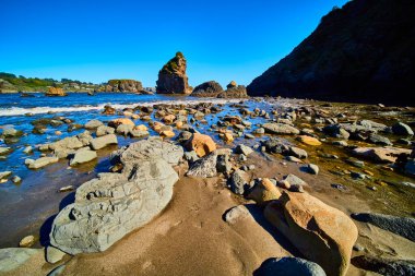 Akşamın ilerleyen saatlerinde Oregon Harris Beach Eyalet Parkı 'nda yosun kaplı taşlar ve heykel şeklinde kaya oluşumları ışıldıyor. Sakin okyanus dalgaları batı kıyısının engebeli kıyı güzelliğini arttırır.