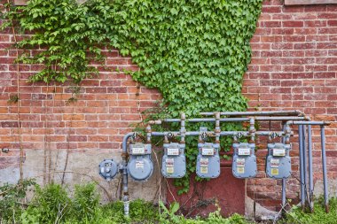 Huntington, Indiana 'da yıpranmış tuğla bir duvarda paslı gaz sayaçları ve gür sarmaşıkların aksine. Görüntü, kentsel bozulma ve dayanıklılık dengesini yakalar, temalar için idealdir