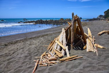 Klamath, California 'daki DeMartin Sahili' nde sakin bir sahil manzarası. Sakin mavi okyanus ve canlı gökyüzü ile, karanlık kum üzerinde sürüklenen ağaç yapısı. Huzur, doğa ve el yapımı güzellik temaları için mükemmel.