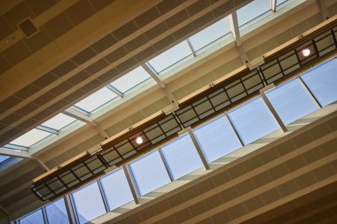 Minneapolis Havaalanı 'nda modern tavan tasarımı, geometrik kirişler, desenli fayanslar ve çatı pencereleri sergileniyor. Doğal ışık filtreleri, yumuşak gölgeler ve temiz, çağdaş