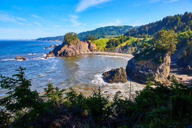 Samuel H. Boardman Eyalet Sahne Koridoru, Oregon 'daki Arch Rock' ın nefes kesici kıyı manzarası. Engebeli uçurumlar, dingin körfez ve berrak mavi gökyüzünün altındaki yemyeşil tepeler doğal güzelliğin simgesidir.