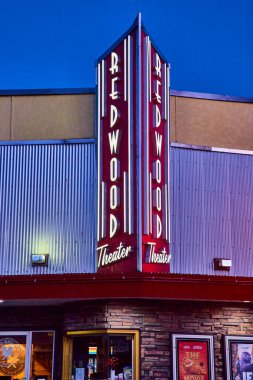 Redwood Tiyatrosunun nostaljik yüzü Brookings, Oregon şehir merkezinde mavi saatte parlıyor. Kalın kırmızı tabela ve neon ışıklar klasik cazibeyi çağrıştırıyor. Canlı bir kent simgesi, modern ve retro ile evleniyor.