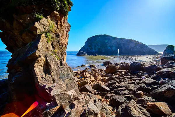 stock image Breathtaking coastal landscape at Harris Beach State Park, Oregon. Rugged stone boulders lead to a stunning natural arch framing a lush, green island. Vivid sunlight enhances the serene beauty of this