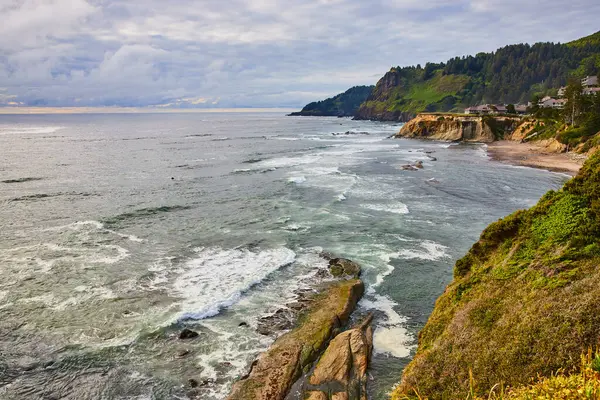 stock image Rugged coastline of Devils Punchbowl, Oregon with lush greenery, dramatic cliffs, and serene waves under a moody sky. Perfect for themes of nature, tranquility, and environmental conservation.