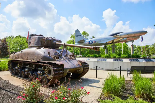 stock image World War II-era tank and vintage jet fighter on display at Charters of Freedom, Huntington, Indiana. A serene park setting contrasts the weathered tank and sleek jet, celebrating military history and