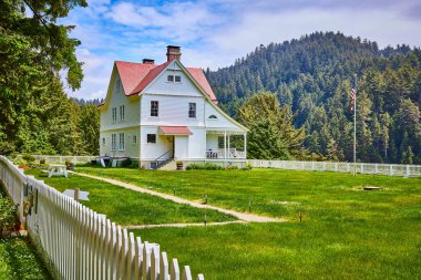 Heceta Head Deniz Feneri, Floransa, Oregon yakınlarındaki yemyeşil kırsal alanda beyaz çatılı ve Amerikan bayrağı olan hoş, klasik bir ev. Aile, ev, kırsal yaşam ve doğa konuları için mükemmel.