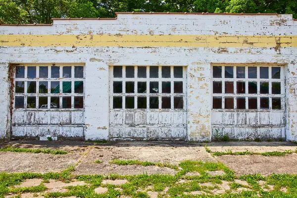 stock image Vintage garage in rural Huntington, Indiana, showcases peeling white paint, cracked glass panes, and a touch of faded yellow, evoking themes of nostalgia and decay against a lush green backdrop.