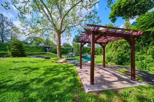 stock image Tranquil scene at Sunken Gardens in Huntington, Indiana: a wooden pergola on a concrete base, lush greenery, a quaint bridge over a pond. Perfect for conveying relaxation, nature, and leisure in a