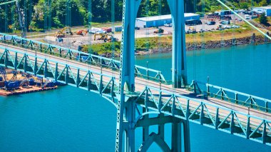 Portland, Oregon 'daki ikonik mercan rengi St. Johns Köprüsü' nün hava manzarası. Endüstriyel bir alana yayılmış geniş bir nehir ve yakınındaki yemyeşil alan. Mühendisliğin mükemmelliğini ve canlılığını gözler önüne seriyor.