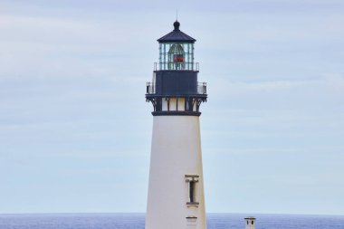 Newport, Oregon 'daki Yaquina Baş Feneri, parıldayan feneriyle, gemilere rehberlik eder. Batıdaki güvenlik ve kararlılığı simgeleyen bulutlu bir gökyüzü ve geniş bir okyanusa karşı dimdik dururlar.