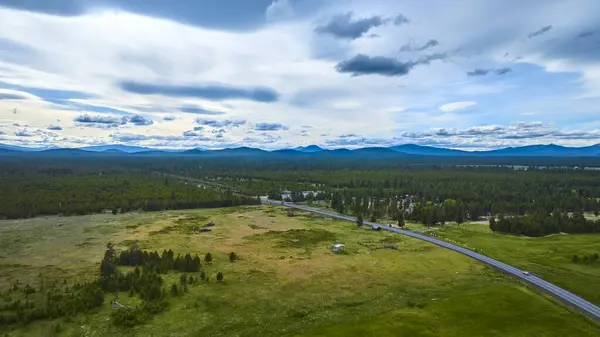 stock image Stunning aerial view of lush green fields and dense forests near Bend, Oregon. A curving highway, distant mountains, and bright blue sky create a serene landscape perfect for travel and nature themes.