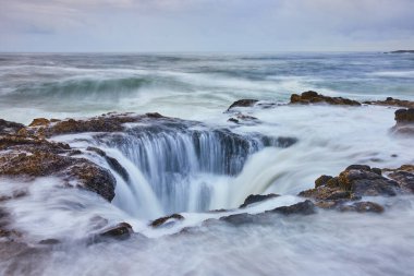 Yachat, Oregon 'daki Majestic Thors Kuyusu' nda Pasifik Okyanusu dalgaları engebeli kayaların üzerinde doğal bir subatana dönüşerek yumuşak ışıkla yıkanmış dingin ve güçlü bir deniz manzarası oluşturur..