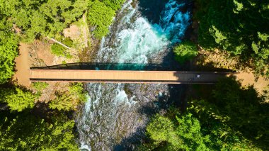 Idleyld Park, Oregon 'daki yemyeşil ormanlarla çevrili akan bir nehrin üzerindeki sakin ahşap köprünün havadan görünüşü. Umpqua Hot 'ın açık hava macerası, sükuneti ve doğal güzelliği için mükemmel.