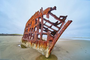 Hammond, Oregon 'da ıssız bir sahilde paslı gemi enkazı Peter Iredale' in ürkütücü manzarası. Çürümüş yapı, zamanın geçişinin ve doğanın gücü ele geçirmesinin bir kanıtı olarak duruyor.