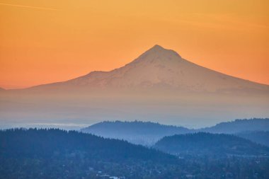 Pittock Malikanesi, Portland 'dan izlenen kar kaplı Mount Hood' un üzerinde nefes kesici bir gün batımı. Sisli, ağaçlık tepelerin katmanları huzurlu, mistik bir manzara yaratarak Oregonların doğal özünü yakalıyor.