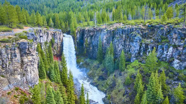 stock image Aerial view of Tumalo Falls cascading down a cliff into a rocky basin, surrounded by lush evergreen forests in Deschutes National Forest, Oregon. Perfect for travel, outdoor adventure, and nature