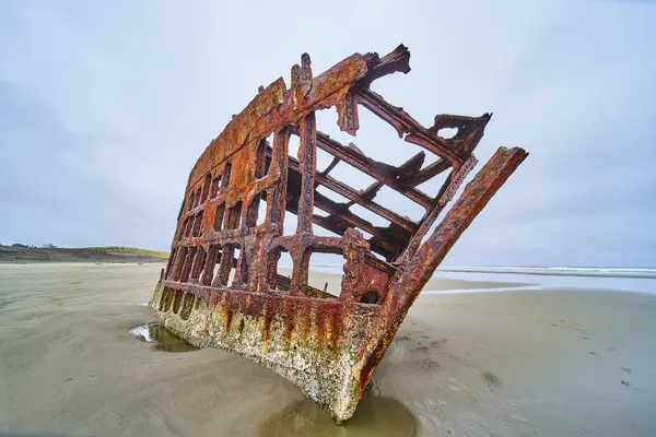 stock image Eerie scene of the rusted shipwreck Peter Iredale on a secluded beach in Hammond, Oregon. The decayed structure stands as a testament to the passage of time and natures reclaiming power against a