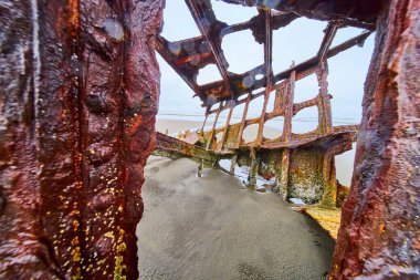 Hammond, Oregon 'un kumlu sahilindeki Peter Iredale gemi enkazının paslı kalıntıları. Çürüyen metal, yumuşak kumlara ve bulutlu gökyüzüne karşı tezat oluşturuyor. Terk edilme ve doğanın temalarını çağrıştırıyor.