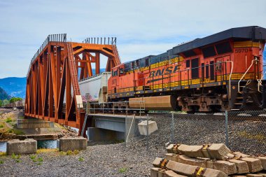 Canlı bir BNSF yük treni Washington 'daki Columbia Vadisi' ndeki rustik Rüzgâr Nehri Köprüsü 'nden Majestic Hills' in arka planına doğru geçiyor. Endüstri, ulaşım ve kırsal konular için mükemmel
