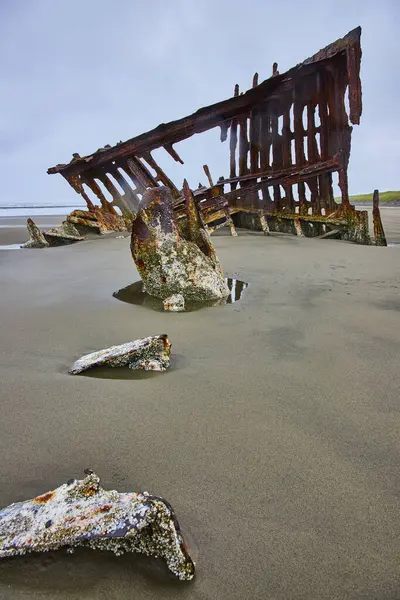 stock image Rusty remains of the Peter Iredale shipwreck on a vast sandy beach in Hammond, Oregon. Stark iron beams and marine growth showcase natures reclamation, evoking themes of decay and the passage of time