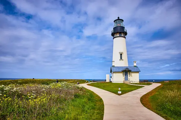 stock image Explore the stunning Yaquina Head Lighthouse in Newport, Oregon. This coastal gem stands tall amidst lush greenery and wildflowers, guiding ships under a serene, partly cloudy sky. Perfect for travel