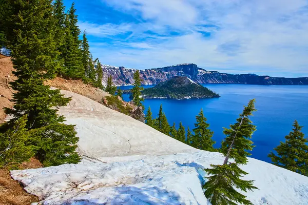 stock image Breathtaking view of Crater Lake in Oregon under a clear blue sky. Pristine deep blue waters, steep cliffs, evergreen trees, and snow create a stunning natural landscape, perfect for nature and