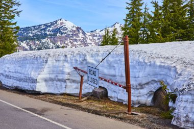 Oregon 'daki Krater Gölü Ulusal Parkı' nda karla kaplı yol tabelası. Etrafını saran devasa kar duvarı ve daima yeşil ağaçlar berrak mavi gökyüzünün altındaki büyüleyici kar örtülü dağlara çarpıyor..