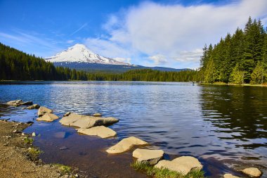 Serene Mount Hood, yemyeşil yemyeşil ve kayalık bir kıyı şeridiyle çevrili sakin bir göle yansıdı. Açık hava maceraları, doğa inzivaları ve Oregon 'a el değmemiş seyahat için mükemmel.