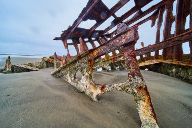 Hammond, Oregon 'da kumlu bir sahilde, Peter Iredale' in paslı gemi enkazı. Çürümüş gemi bulutlu bir gökyüzüne karşı tarihi ve doğa eserlerini geri istiyor..