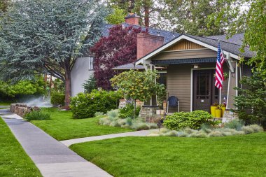 Charming Bend, Oregon 'daki evinde Amerikan bayrağı, bakımlı çimenler ve verandada canlı bitkiler var. Banliyöde yaşamanın, mahalle gururunun ve Amerikan rüyasının mükemmel bir fotoğrafı..