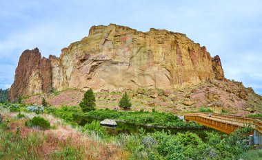 Huzurlu nehir ve yemyeşil yeşil çerçeve Oregon 'daki Smith Rock State Park' ın görkemli kaya oluşumları. Tahta bir köprü, insan işçiliğini doğal güzellikle harmanlayarak keşfi davet eder. Mükemmel.