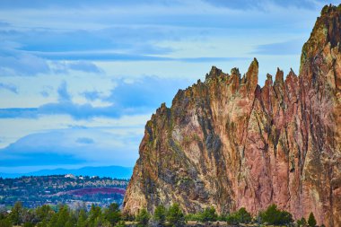 Terrebonne, Oregon 'daki Smith Rock State Park' ın görkemli uçurumları dinamik bir gökyüzü altında yükseliyor. Engebeli oluşumlar canlı kırmızılar, kahverengiler ve yeşillikler sergiliyor, çarpıcı bir doğal mimari ortaya koyuyor.