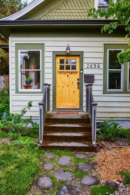 Portland, Oregon 'da açık yeşil bir ev. İçinde cam pencereli, yemyeşil bahçeli ve taş yolu olan sıcak sarı bir kapı var. Ev, aile ve konut mimarisi temaları için ideal.