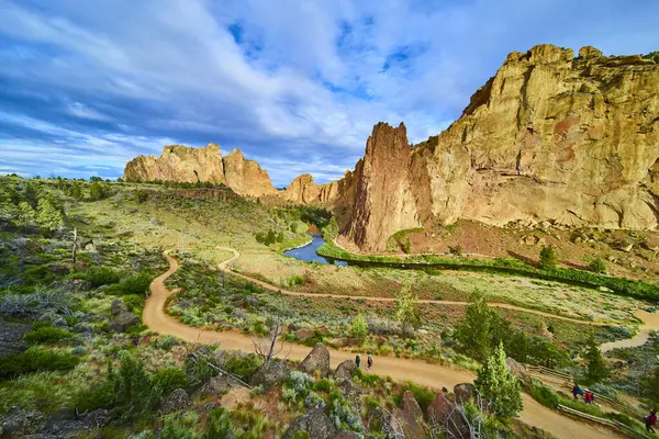Yürüyüşçüler Oregon 'daki Smith Rock State Park' ın manzaralı patikalarını keşfediyorlar. Kırmızımsı kahverengi kayalıklar, yemyeşil yemyeşil ve dolambaçlı bir nehir resim gibi bir gökyüzünün altında nefes kesici bir zemin oluşturur.