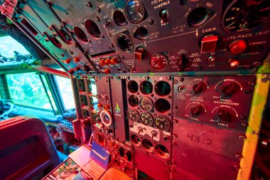 Karmaşık gösterge ve düğmeleri olan klasik uçak kontrol paneline yakın plan, kırmızı ortam ışığıyla yıkanmış. Portland, Oregon 'daki Airplane House' da yakalanan bu görüntü nostalji ve teknolojiyi çağrıştırıyor.