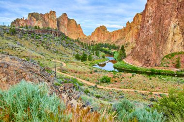 Smith Rock State Park, Oregon 'un sakin manzarası. Sakin bir nehir, yüksek uçurumlar ve yol boyunca yemyeşil yemyeşil olan dramatik kanyonlarda süzülür. Seyahat ve macera temaları için mükemmel.