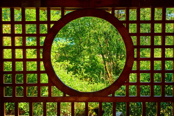 stock image Circular wooden window frames a lush, green landscape at Gresham Japanese Garden, Oregon. The serene garden scene highlights the harmony between traditional architecture and nature, evoking peace and