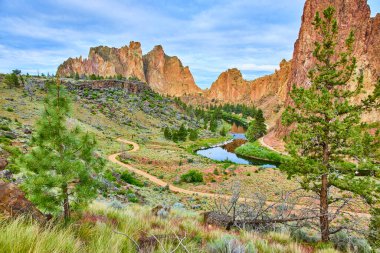 Oregon 'daki Smith Rock State Park' ın çarpıcı güzelliğini keşfedin. Pürüzsüz kaya oluşumları ve yemyeşil yemyeşil ile çevrili yol boyunca sakin bir nehir manzarayı yansıtıyor..