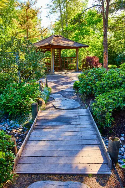 stock image Serene garden path leads to a wooden gazebo in Gresham Japanese Garden, Oregon. Surrounded by lush greenery and vibrant sunlight, this tranquil retreat invites relaxation and nature appreciation.