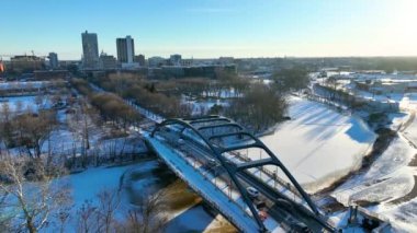 Fort Wayne, Indiana 'nın ikonik Martin Luther King Köprüsü ve karla kaplı Gezinti Parkı' nı gösteren hava manzarası. Büyüleyici şehir manzarası altın saat ışığıyla yıkandı, kenti harmanladı.