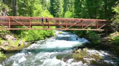 Aerial Fly Through Forward: Oregon 'daki Umpqua Hot Springs' in sakinliğini tecrübe edin. Resimli yürüyen bir köprünün üzerinde süzül, dinamik akan bir nehir, ve yemyeşil ormanlar, huzurlu ormanı yakalıyor.